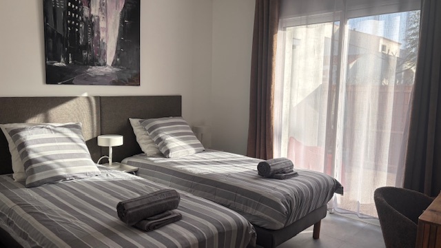 Chambre Lagune Chambre lumineuse avec deux lits jumeaux, décor minimaliste et rideaux clairs.