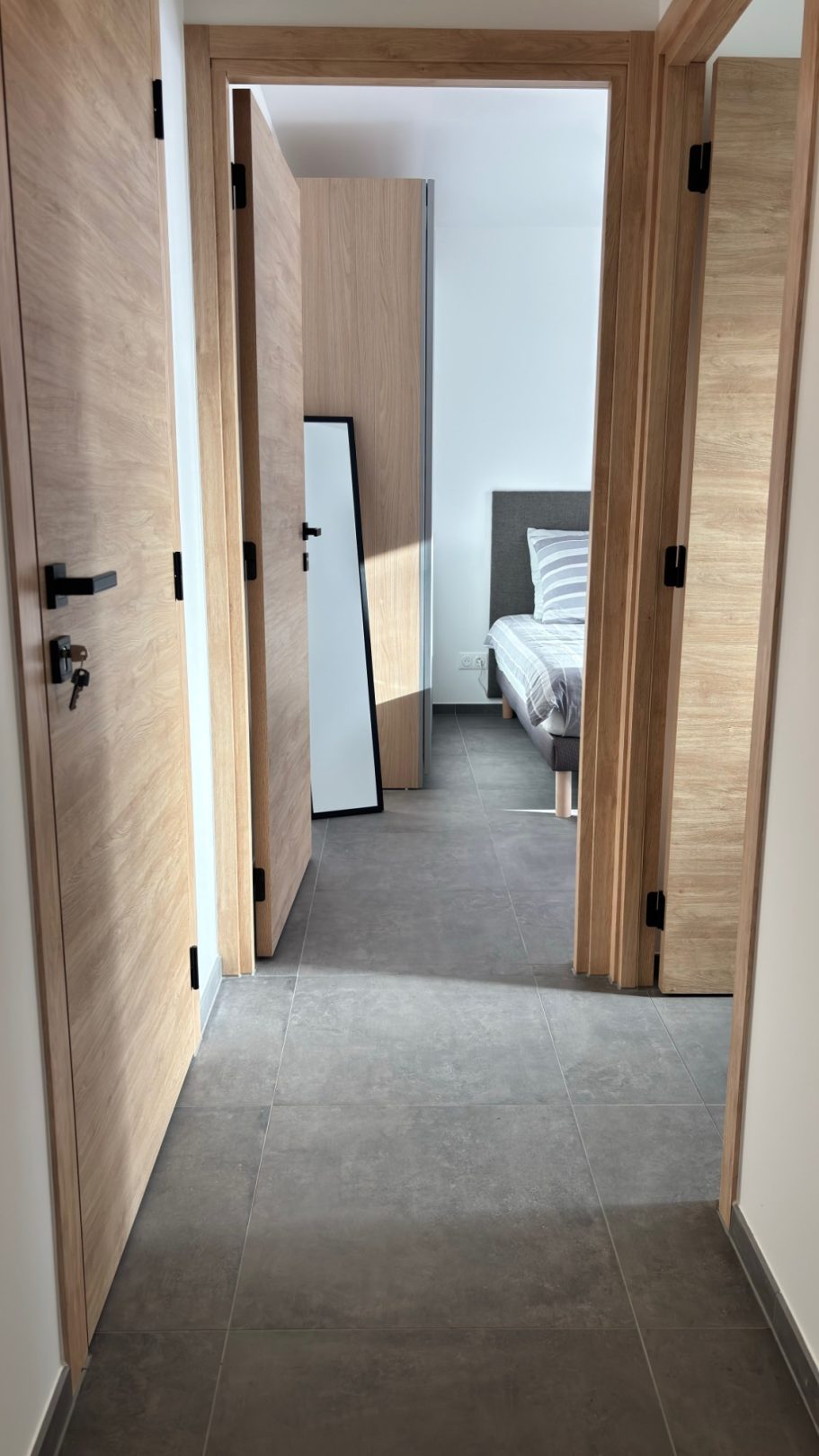 Couloir lumineux avec deux portes ouvertes menant à une chambre et un miroir.