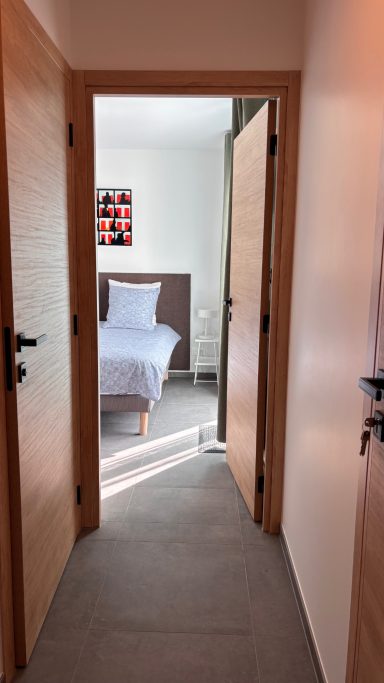 Chambre l'olivier Vue d'un couloir menant à une chambre avec lit et décoration murale colorée.